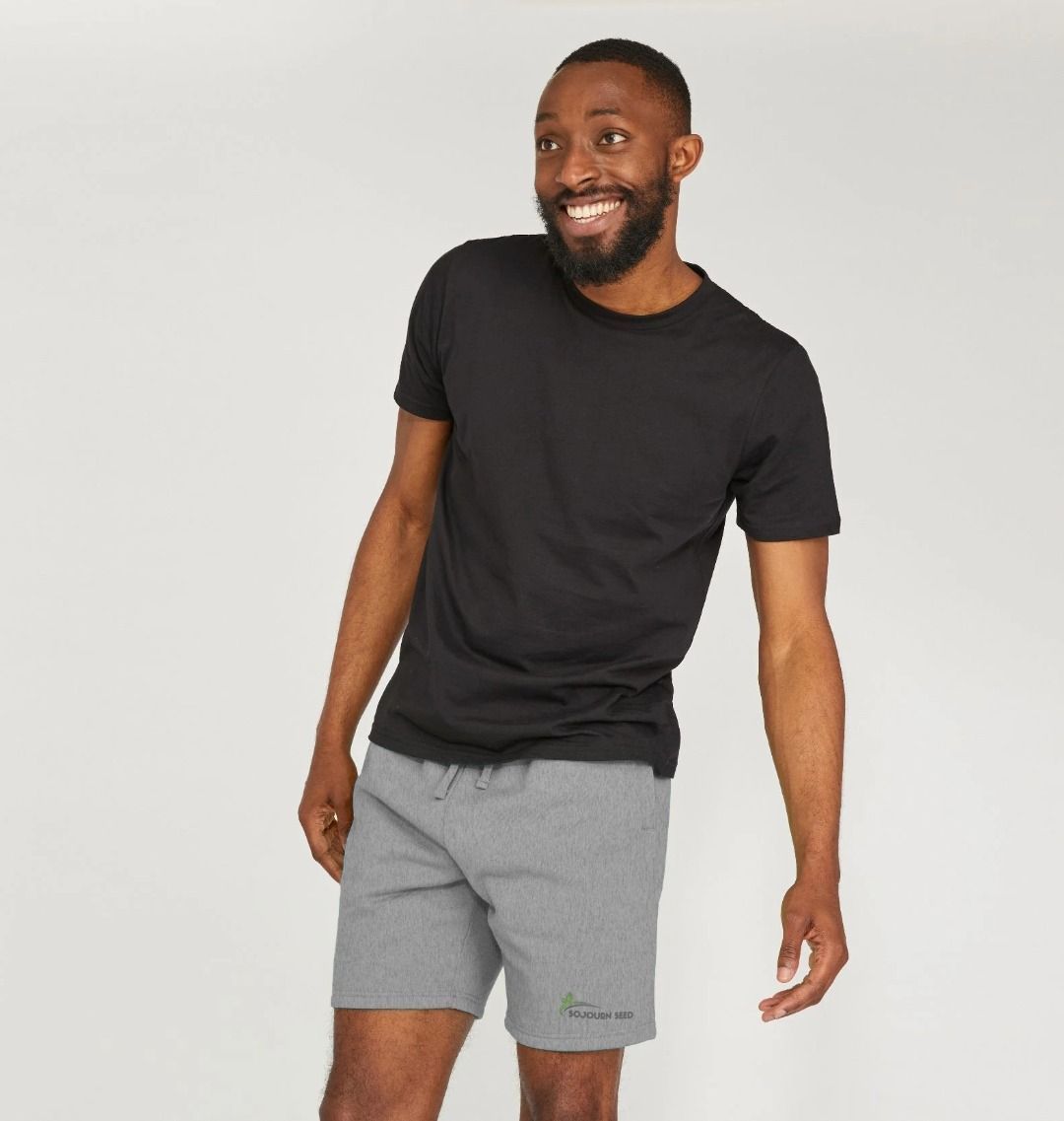 Smiling man wearing comfortable men's apparel in a black t-shirt and gray shorts against a plain background