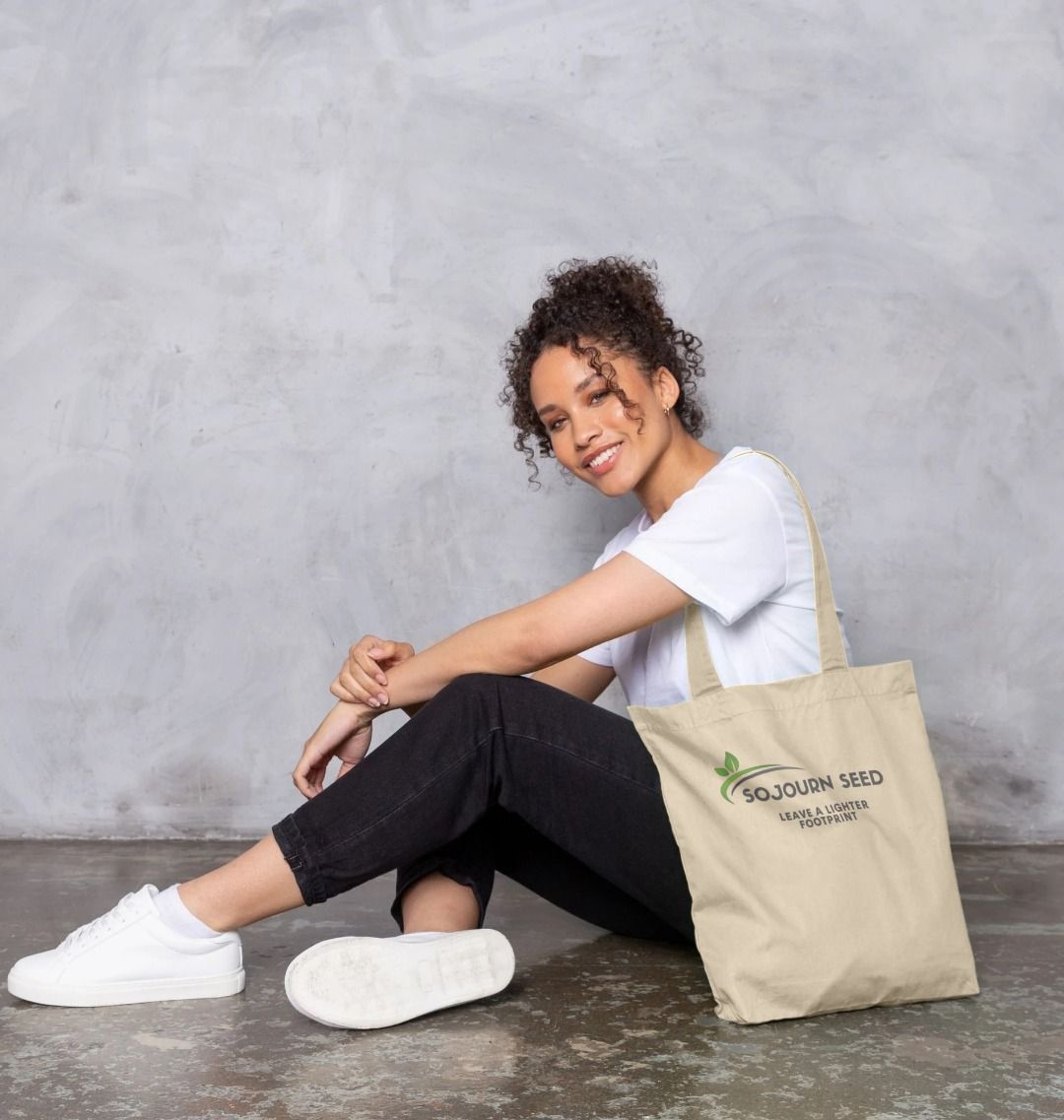 Smiling woman sitting wearing an organic cotton tote bag printed with Sojourn Seed logo and text