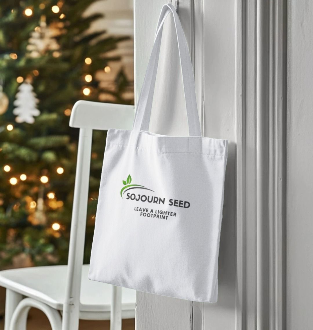 Sojourn Seed organic cotton tote bag with green logo and eco-friendly message hanging on a white door