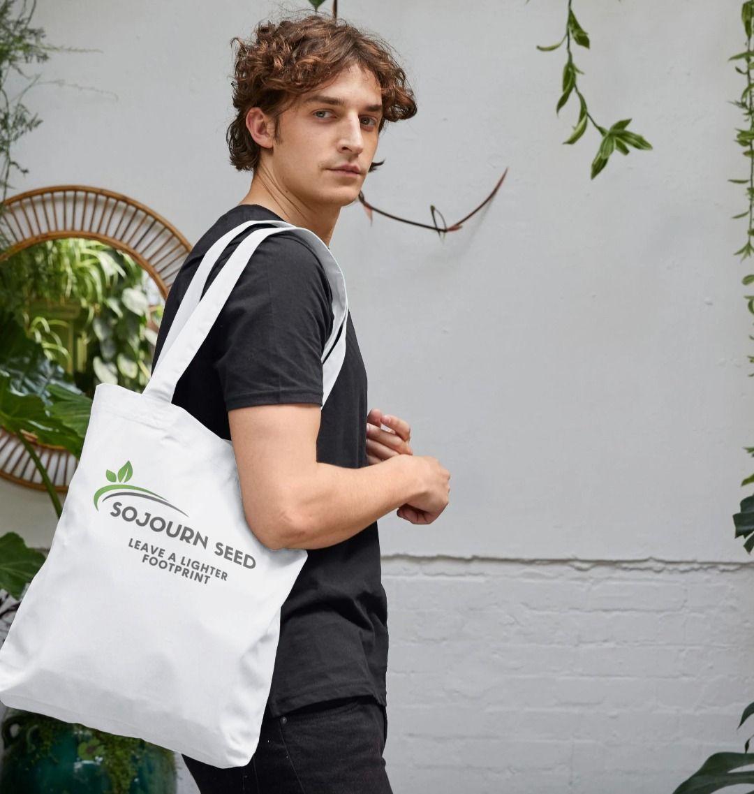 Sojourn Seed printed organic cotton tote bag carried by man in black shirt with eco-friendly message