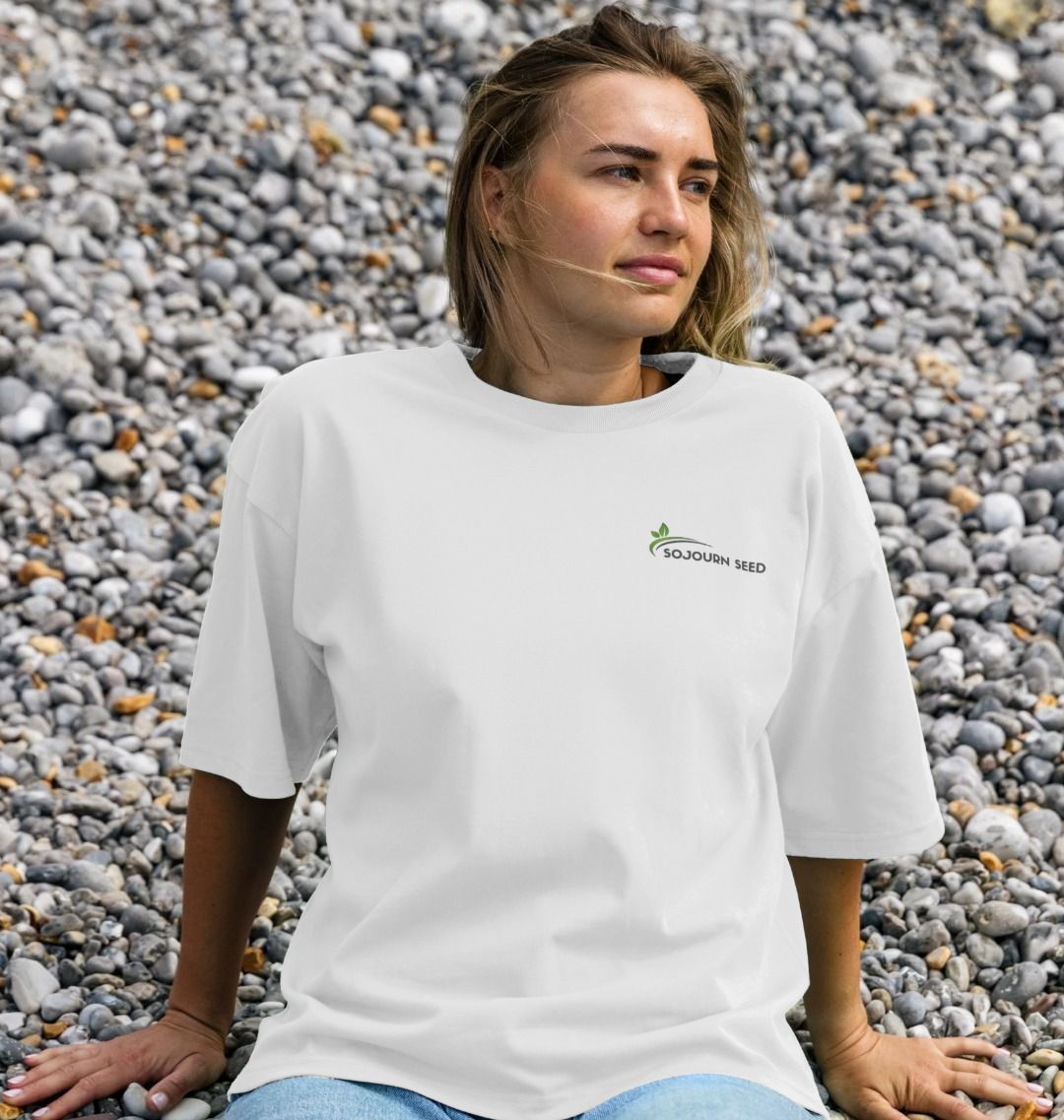 Sojourn Seed printed organic women's t-shirt in white worn by woman sitting on rocky beach